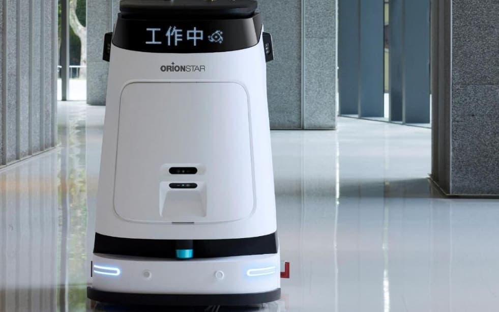 Un robot de nettoyage autonome, blanc et noir, qui avance sur le sol brillant d’une galerie