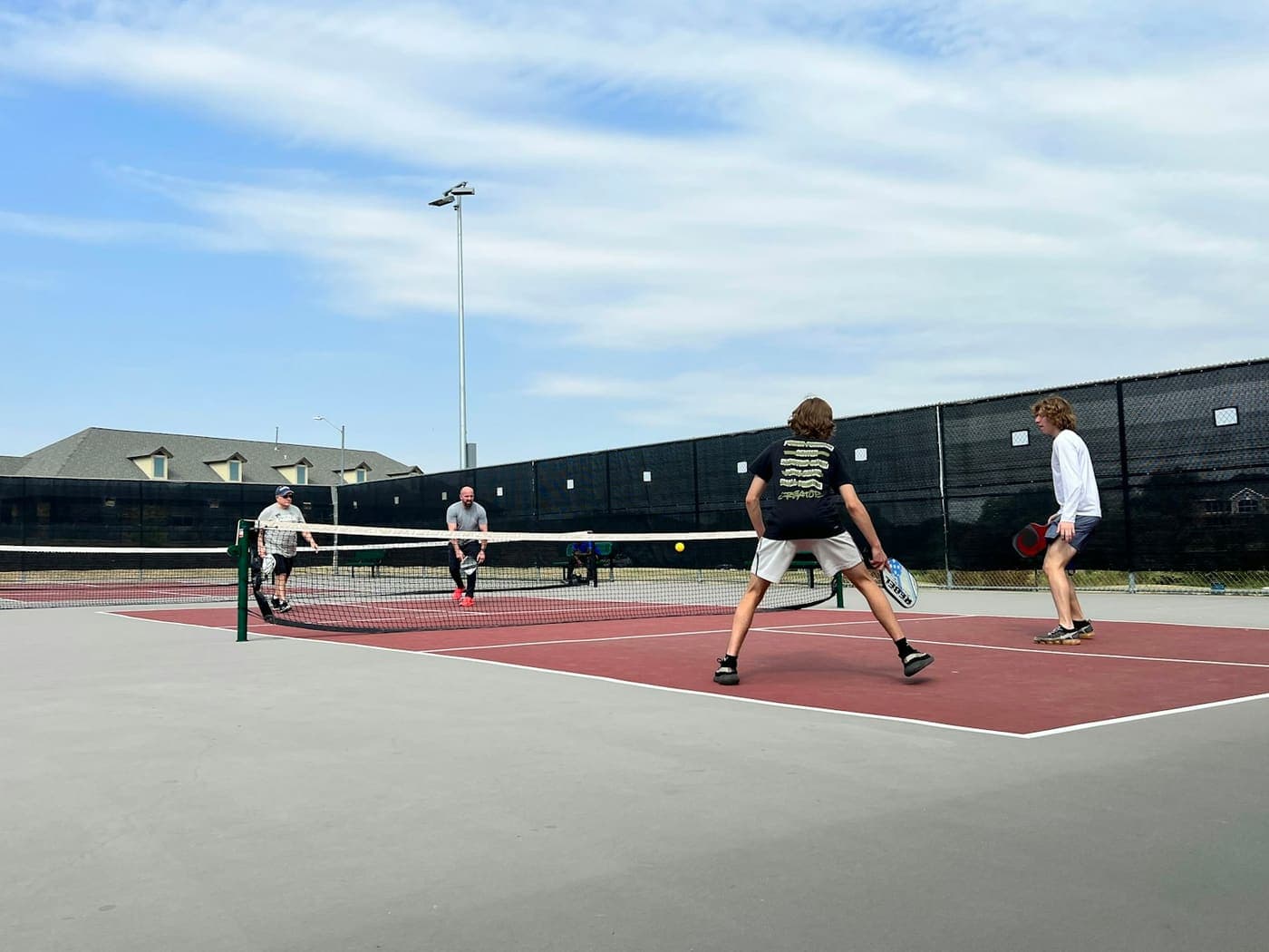 Une partie de pickleball en double sur un terrain extérieur, quatre joueurs de part et d’autre du filet