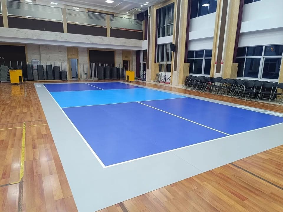 Un terrain de pickleball mobile, bleu à lignes blanches, posé sur le parquet d’un gymnase