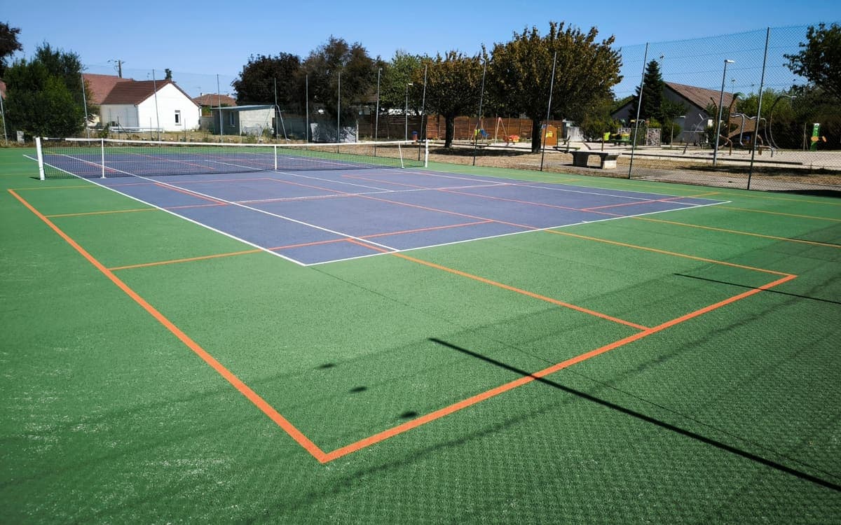 Un court de tennis extérieur sur lequel des terrains de pickleball ont été tracés : lignes orange autour des lignes blanches du tennis